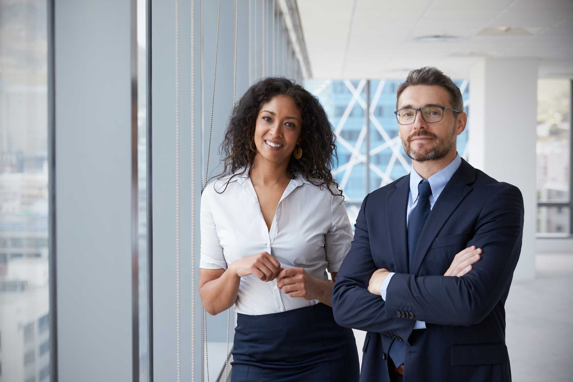 Two professionals standing side by side, dressed in business attire and smiling