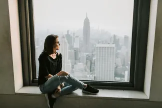 Woman gazing out the window of a tall building, overlooking a cityscape below