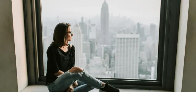 Woman gazing out the window of a tall building, overlooking a cityscape below